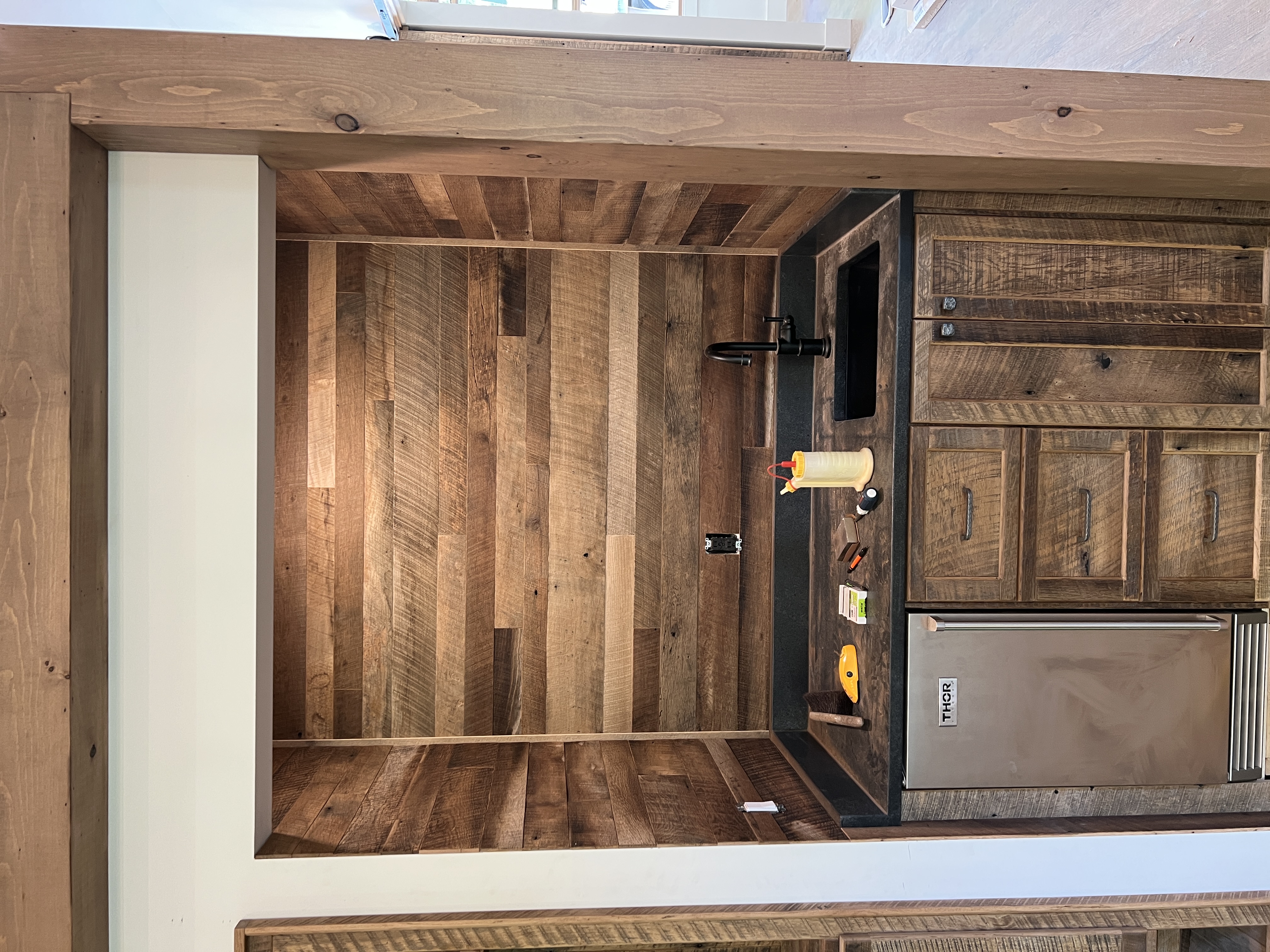 Reclaimed wood wet bar niche close-up with black countertop and Thor mini fridge
